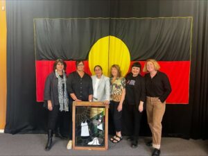 Event participants standing. In front of them is the stain glass artwork, and behind them, the Aboriginal flag.