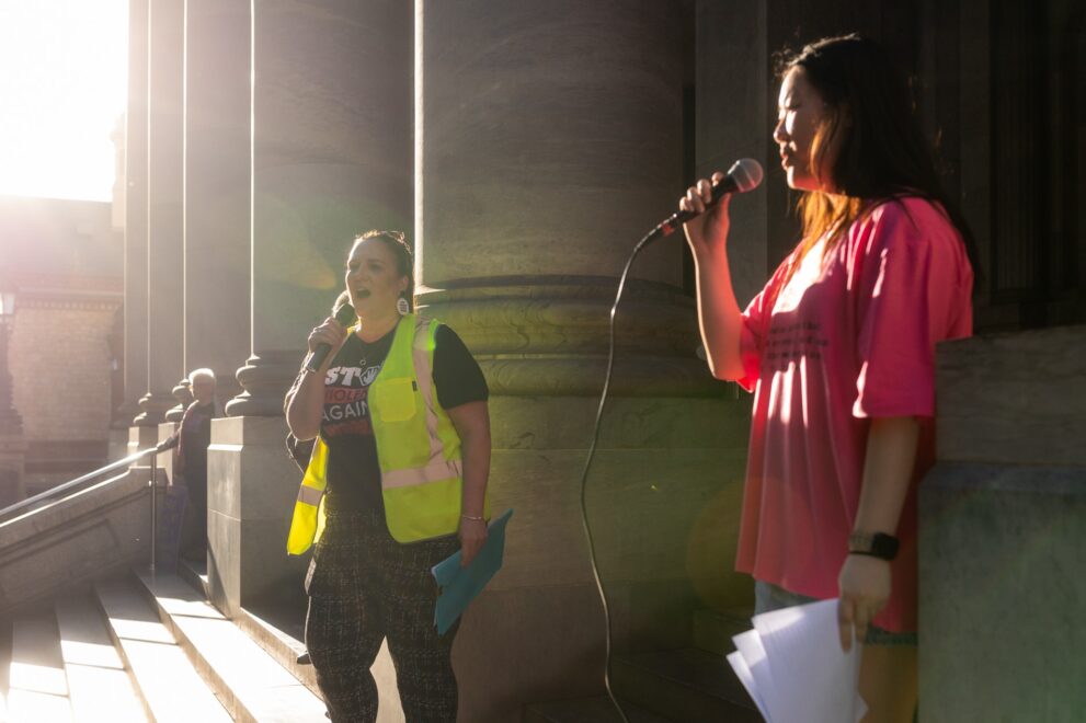 Two people standing on the steps of parliament house, speaking in to microphones.