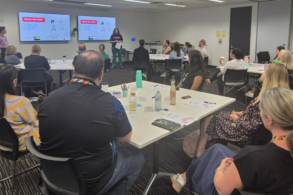Working Women’s Centre facilitators deliver a workplace training session to a group of participants seated around tables in a training room.